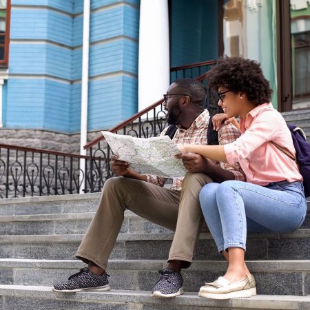 Two people sat on a building outdoor stairs. The are looking at a map